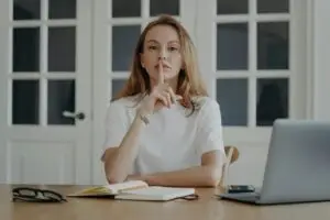 Lady gestures hush in concept of secret and privacy. Young businesswoman is working from home.