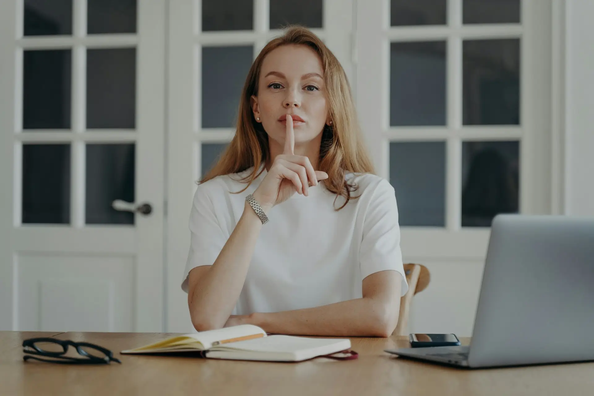 Lady gestures hush in concept of secret and privacy. Young businesswoman is working from home.
